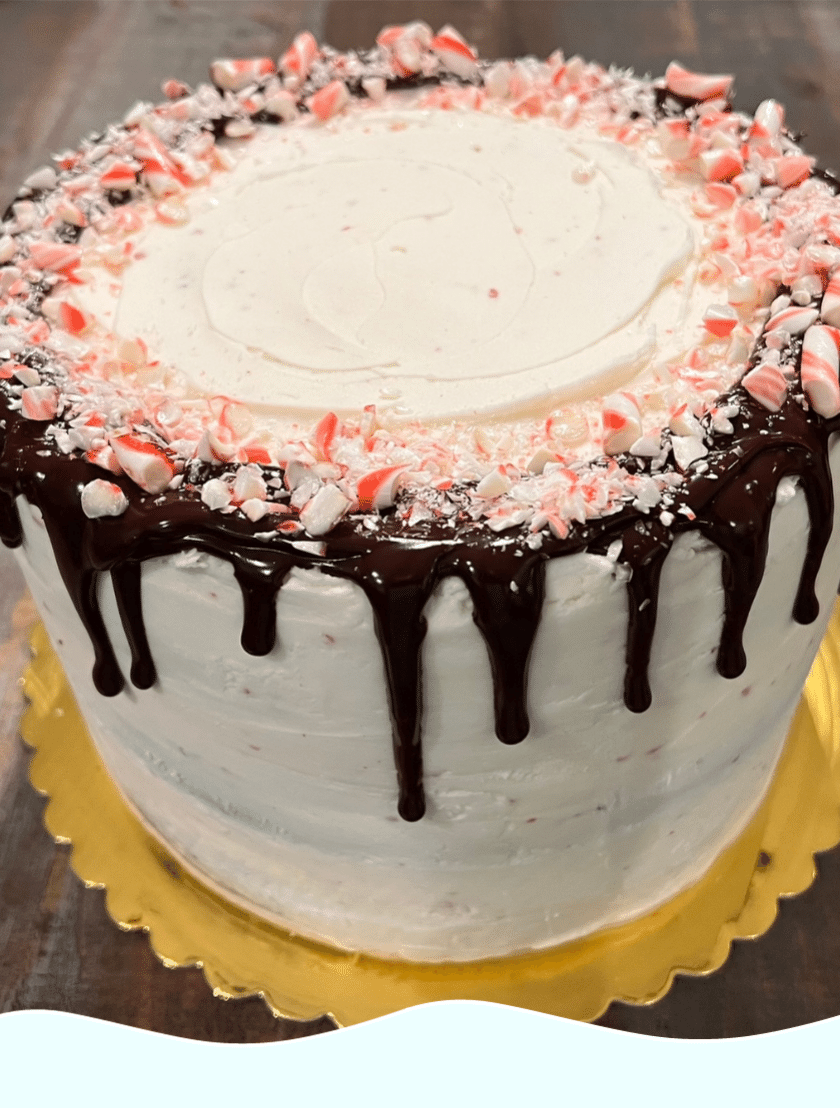 Gluten free cake with white frosting, a chocolate drizzle, and candy cane crumbles